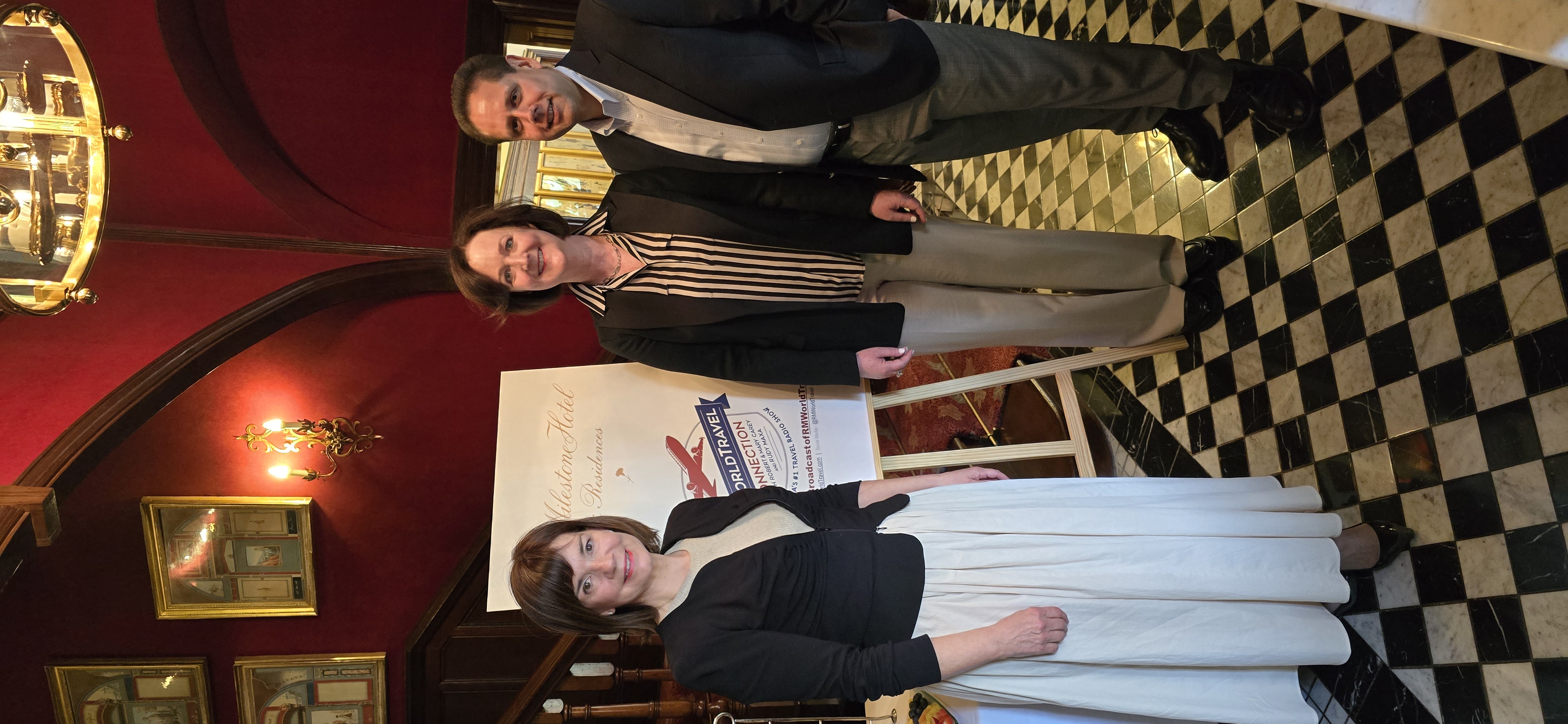 Three professionals posing by World Travel Connection sign in elegant Milestone Hotel lobby with red walls, checkered floor
