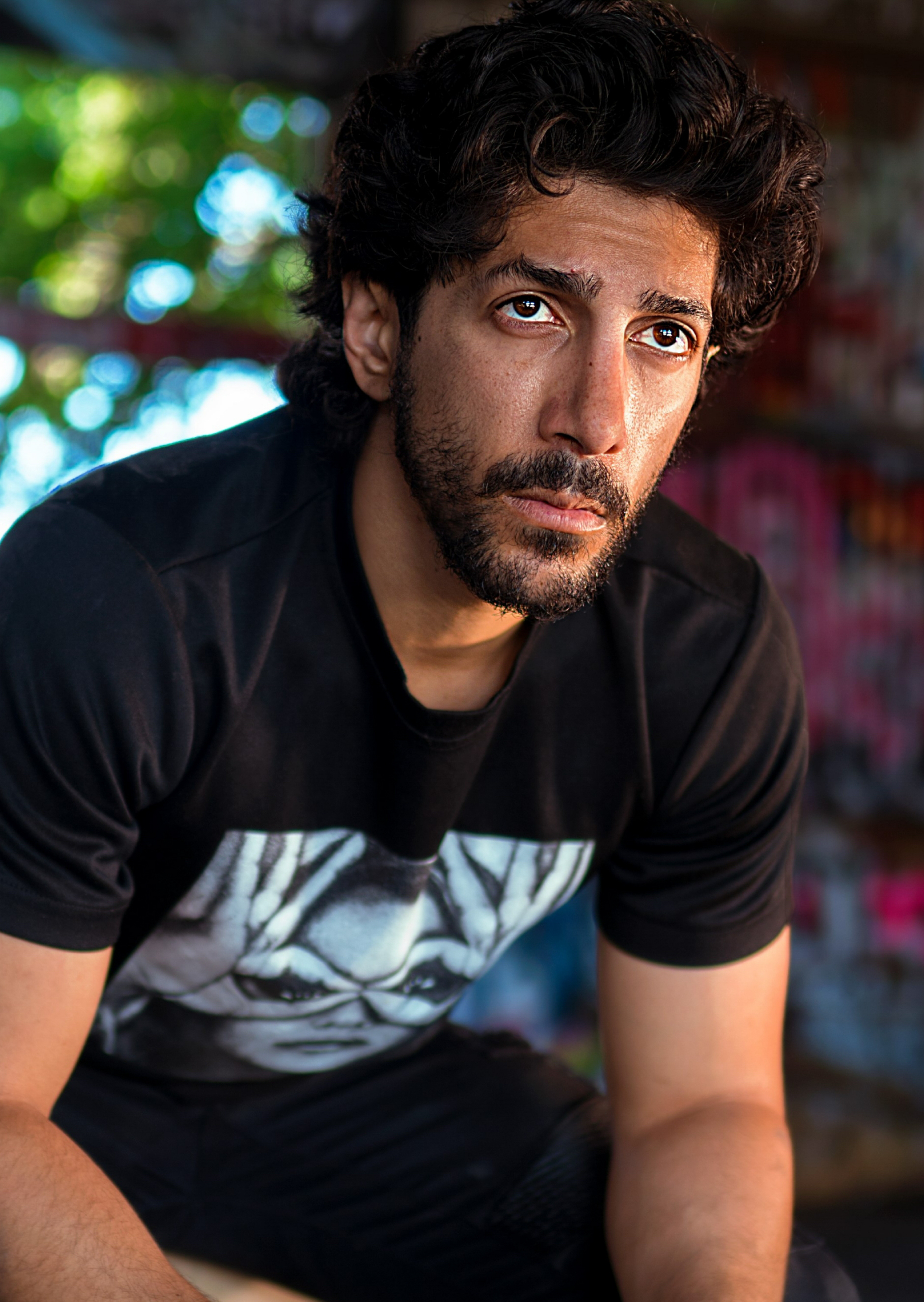 Close-up portrait of pensive bearded man in black t-shirt, urban bokeh background