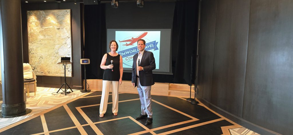 Two presenters holding microphones on stage at travel conference with logo projected, modern conference room