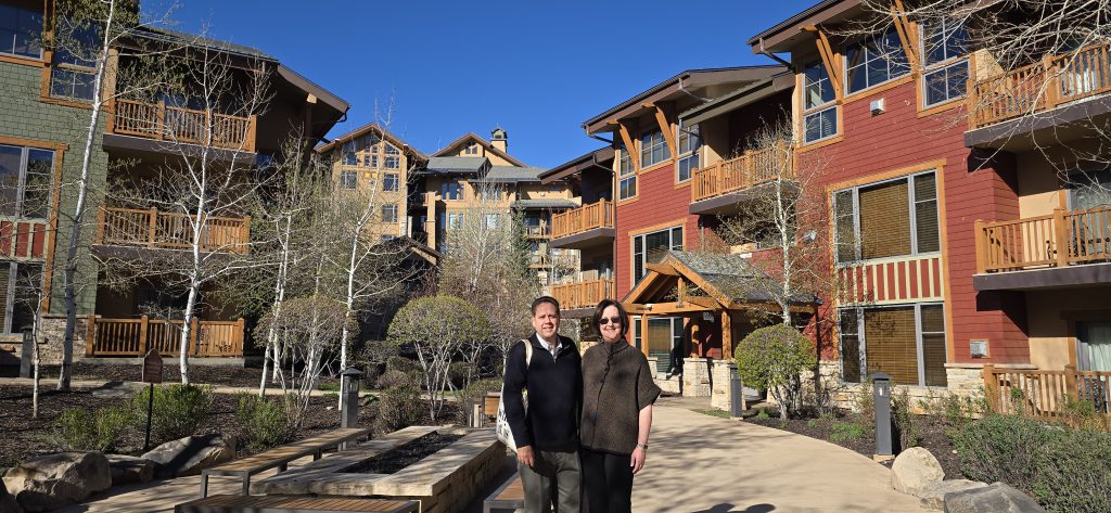 Couple standing outside colorful mountain-lodge condos with wooden balconies under clear blue sky