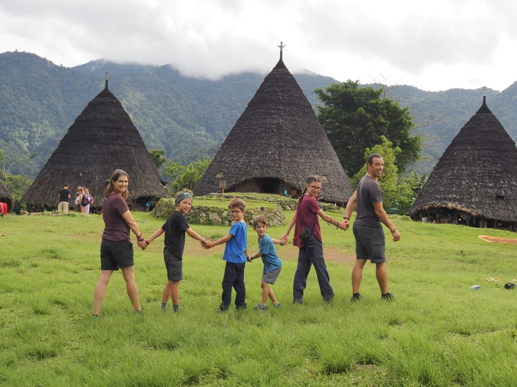 Smiling family holding hands in front of traditional conical thatched huts in a lush mountain village