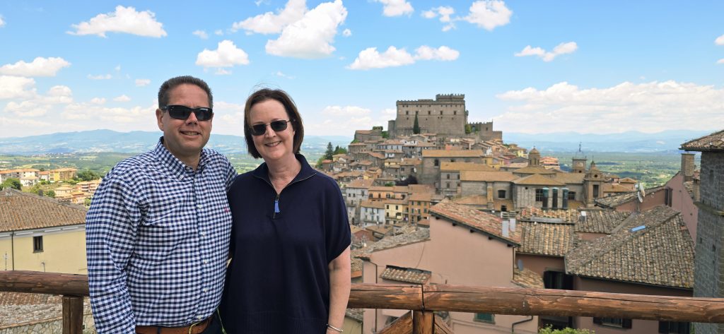 Tourist couple on terrace overlooking medieval Italian hilltown and fortress castle with panoramic countryside view