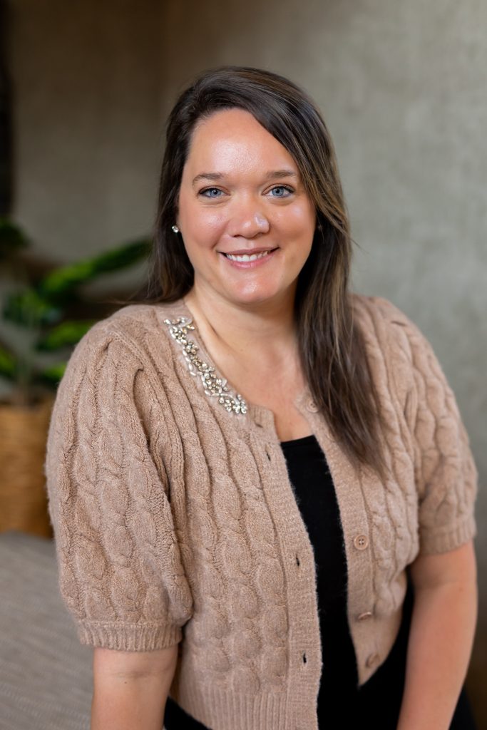 Smiling woman headshot wearing beige cable-knit cardigan with jeweled neckline, neutral indoor background