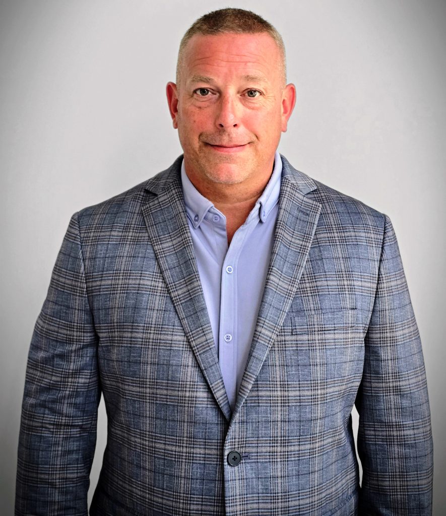 Professional headshot of a smiling businessman in a gray plaid blazer and light blue shirt, neutral background