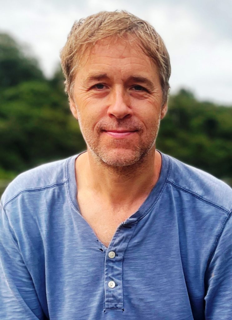 Smiling middle-aged man portrait in casual blue henley shirt outdoors with blurred green nature background