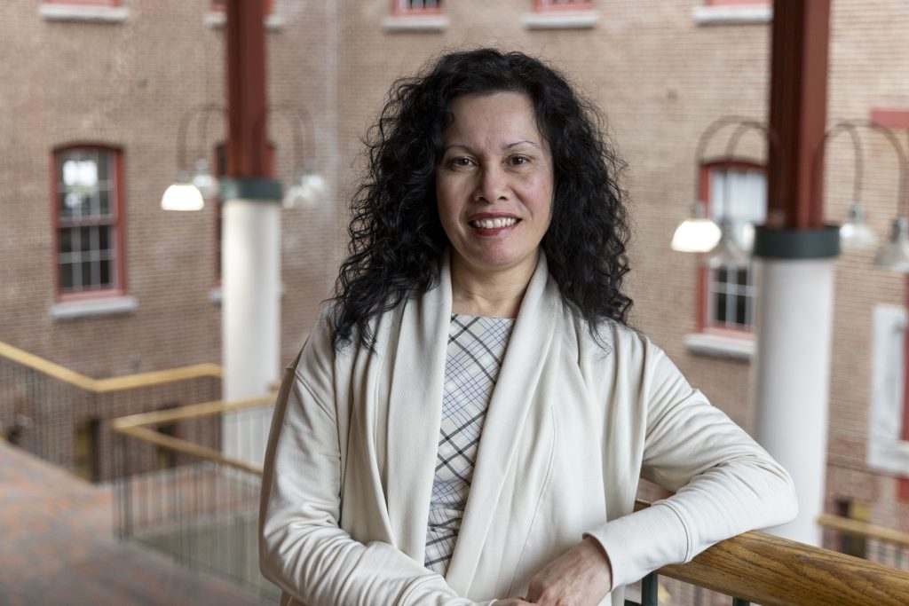 Professional portrait of smiling businesswoman with curly black hair wearing cream jacket in brick atrium